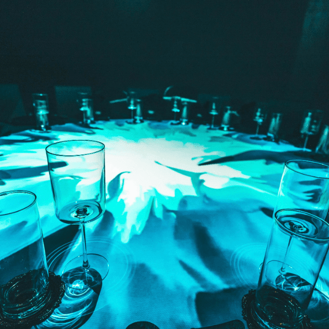 round table surrounded with wine glasses and projection mapping on surface of table